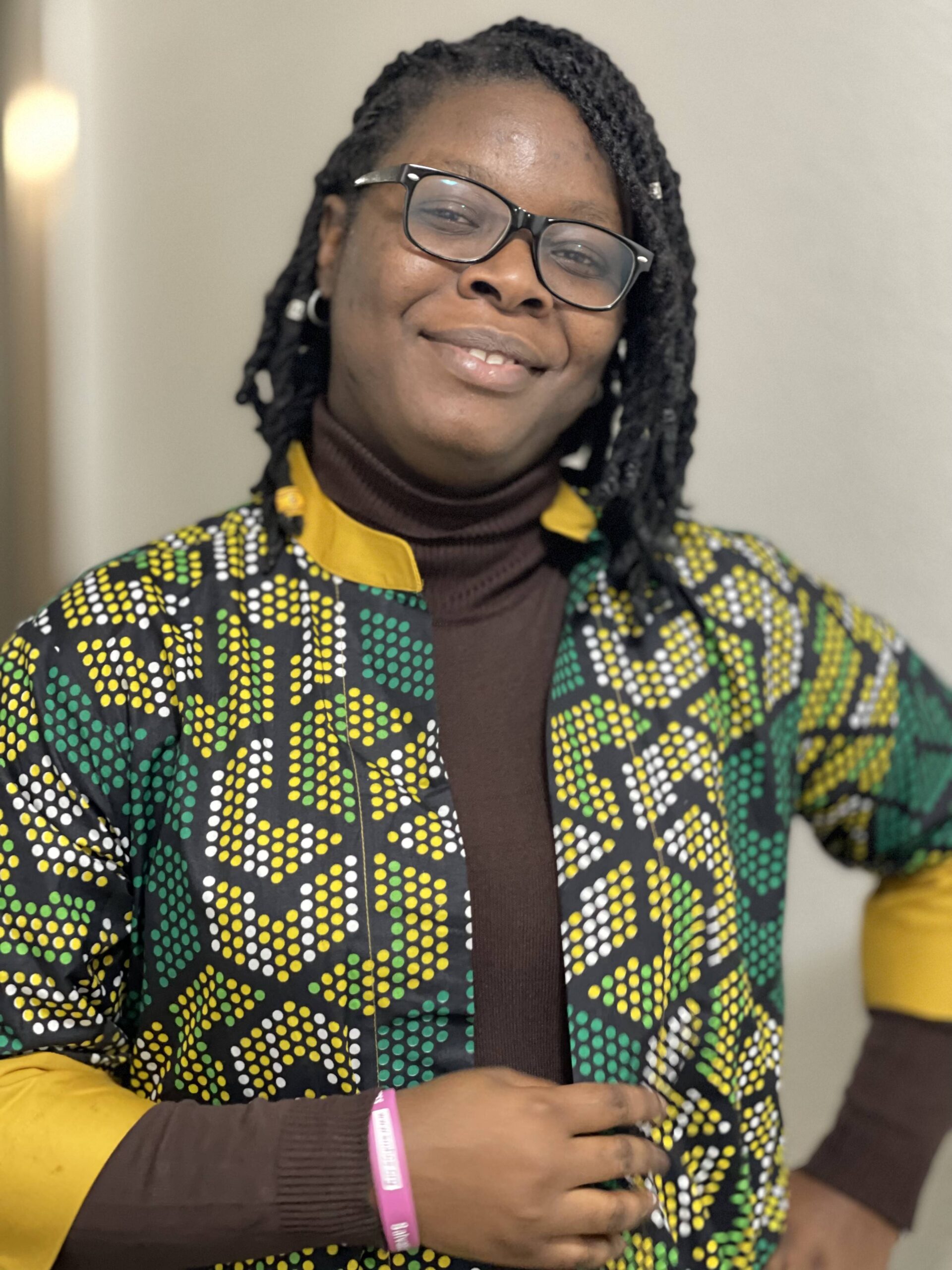 image of Peggy CEO Jejelove Solutions, tall ebonyskinned lady with locs on her head and a pair of eyeglasses on her face, standing with one hand akimbo with a small smile on her face.
